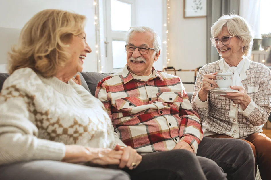Seniors have tea on couch in festive clothing with twinkle lights in the background.
