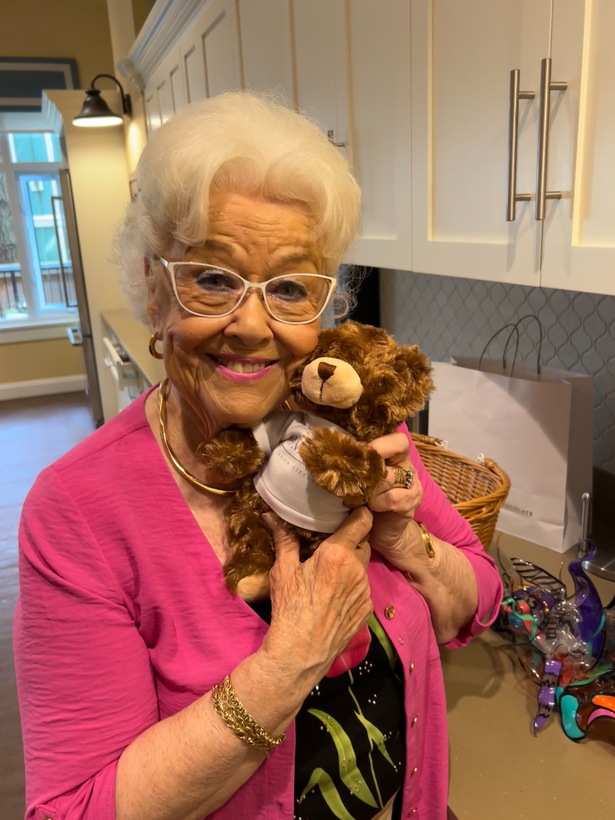 Pat, an Amica resident who leads a craft program, holds a teddy bear to her face, smiling.