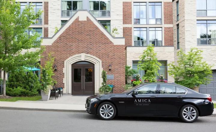 Exterior shot of Amica On The Avenue's entrance area, with an Amica branded black car parked in front of the residence. 
