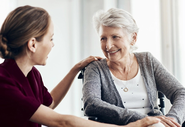 KER-Additional Memory Care A caregiver gently placing a hand on the shoulder of a smiling senior woman seated in a wheelchair