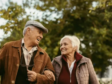 Senior couple walks arm in arm Senior couple walks arm in arm among trees on a clear day.