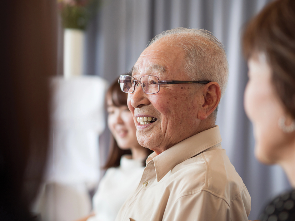 Senior man, who seems to be surrounded by family in the background, smiles