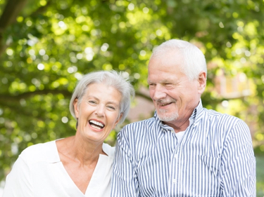 A senior souple smile among the trees while standing side by side.