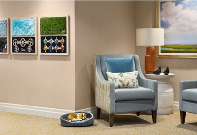 Textile art is hanging in a hallway alongside an inviting chair and lamp.