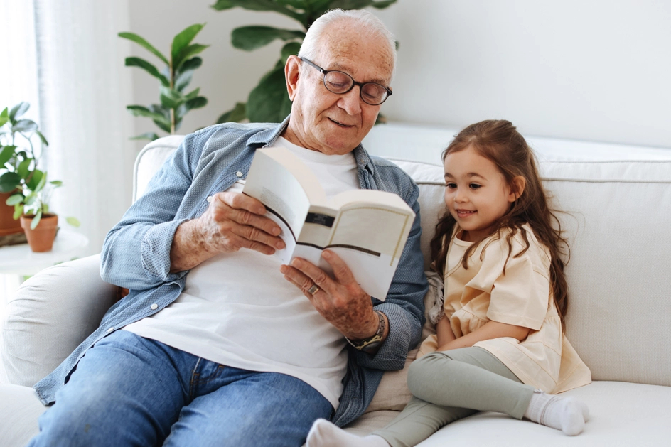 A shot of a senior reading a book to a child, sitting on a couch