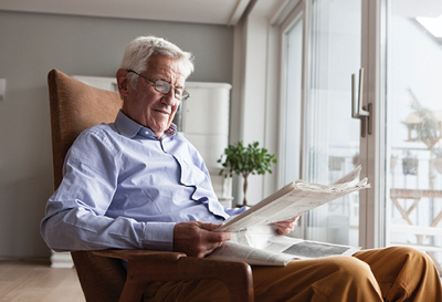 Senior reads his paper in a chair by the patio doors