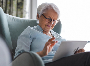 seniorwomanlookingatipadsittingonachair-mobilebanner