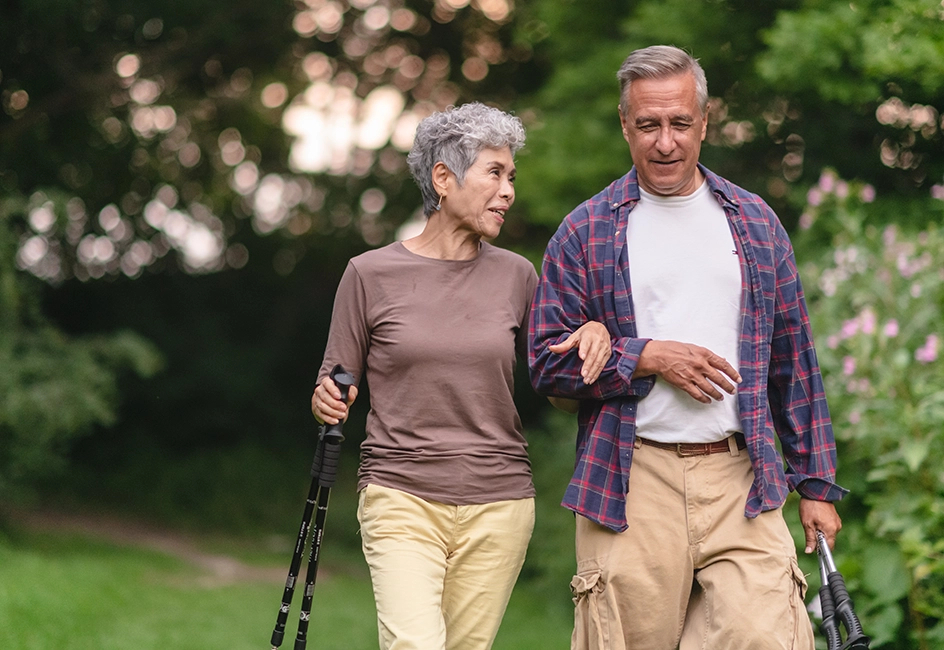 Seniors walk outside arm in arm. They're walking on a pathway framed by lush greenery.