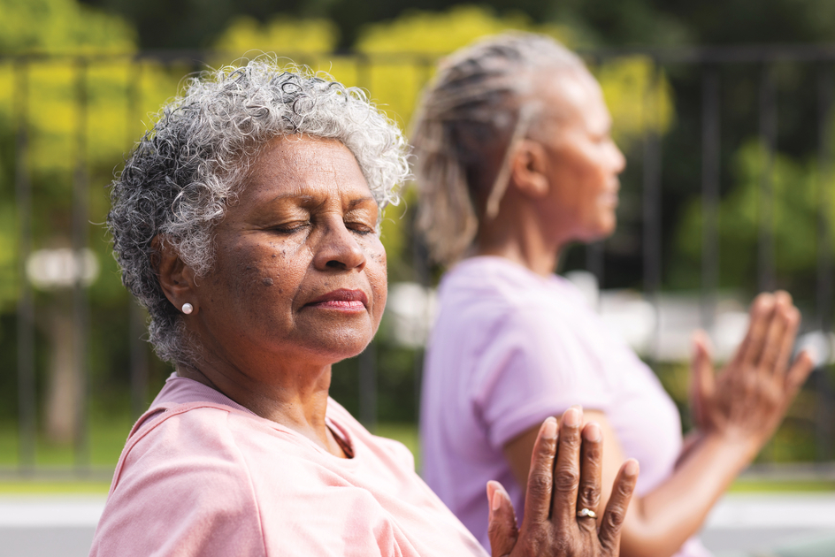 Women sit with eyes closed doing a yoga pose