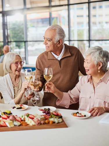 A trio of seniors enjoy a wine tasting, which is being led by a waiter.