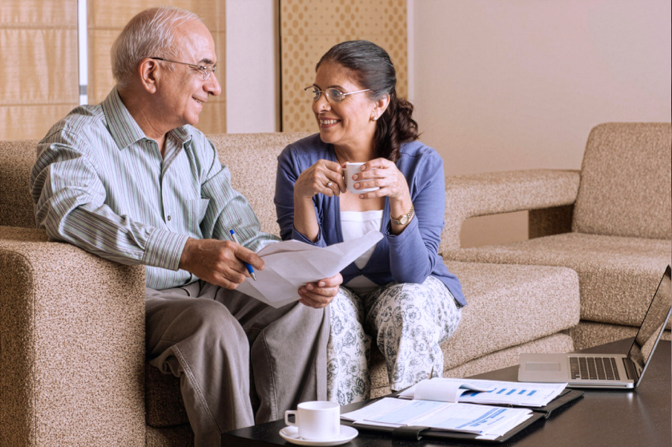 A senior couple seated on a couch looking over paperwork.