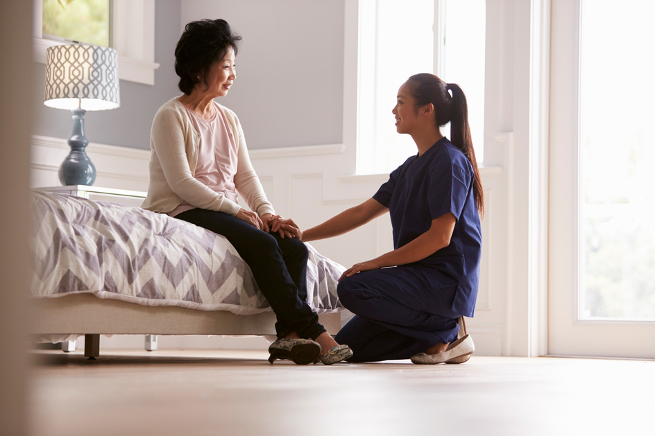 An Amica employee holds the hand of a senior who's sitting on a couch.
