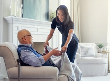Female resident placing blanket over male resident in chair