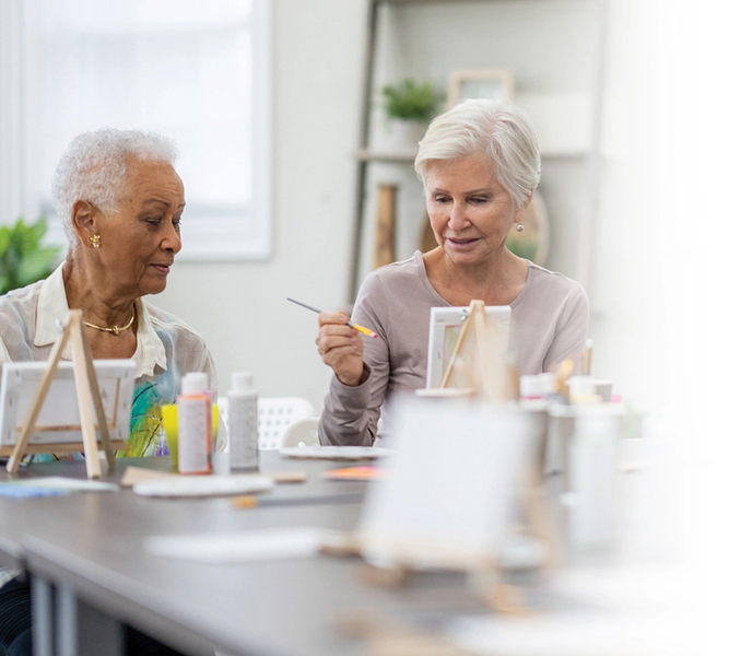 Senior women paint together on small easels at a table.