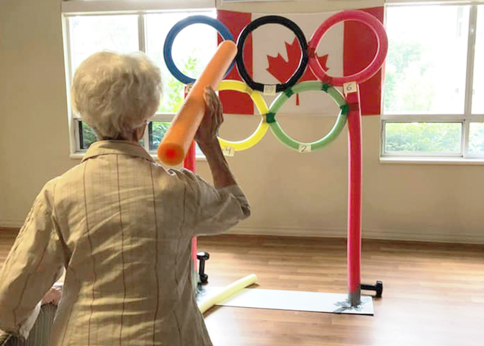 A senior woman playing an Olympic activity game about to throw an orange pool noodle.