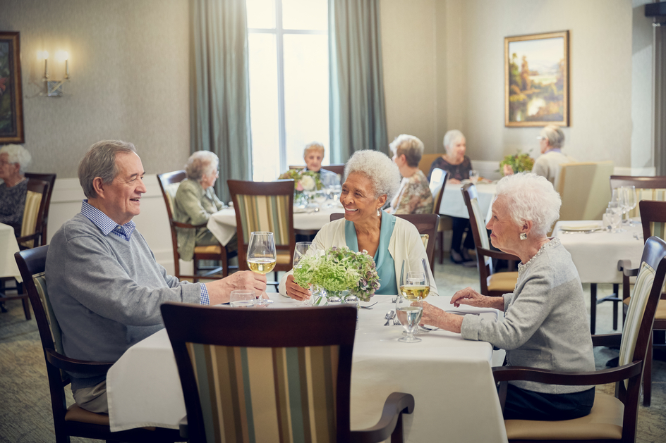 Three residents enjoying conversation and white wine at table in residence dining room