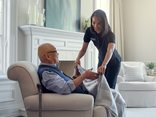 Female resident placing blanket over male resident in chair