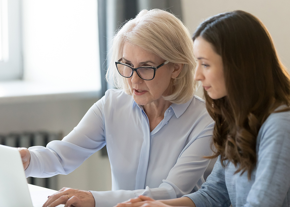 A senior woman and her daughter working on a white laptop.