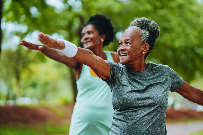 Two women stretch out their arms, as they stand amid trees outside.