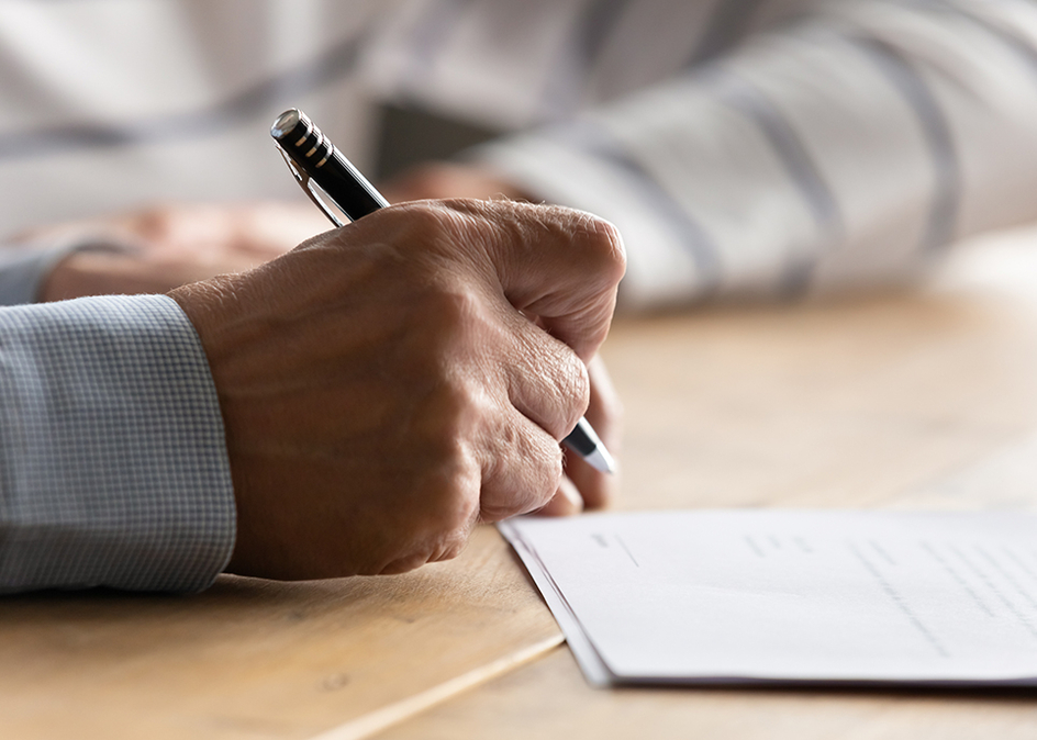 A close up of a senior holding a pen and about to sign a document.