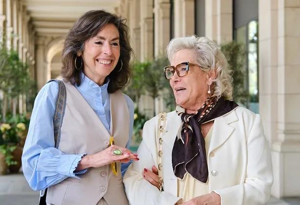 Woman walks arm-in-arm with senior in columned courtyard.