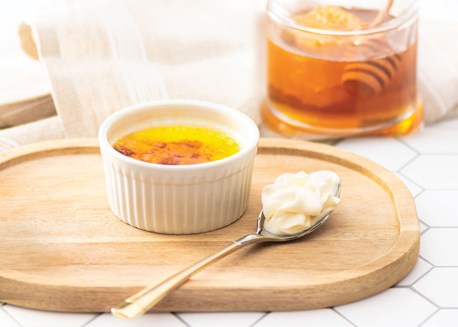 Honey creme brulee on top of a wooden serving tray with a jar of honey in the background