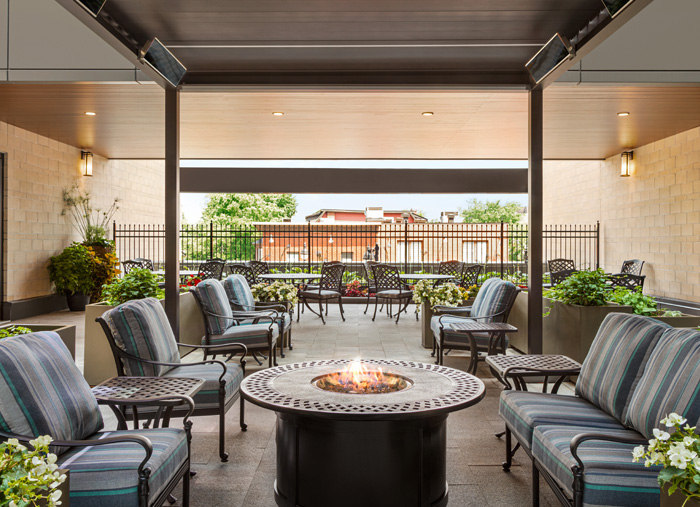 A view of the Amica Glebe terrace. Plush outside furniture surrounds a sleek firepit under outdoor roofing.