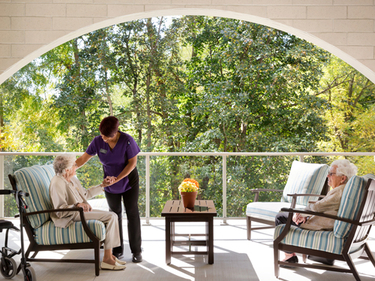 Two senior women and a caregiver are enjoying a bright sunny afternoon on the main floor terrace's couches.