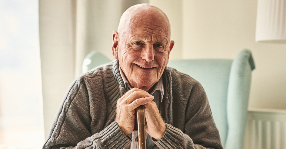Portrait of happy senior man sitting at home with walking stick and smiling