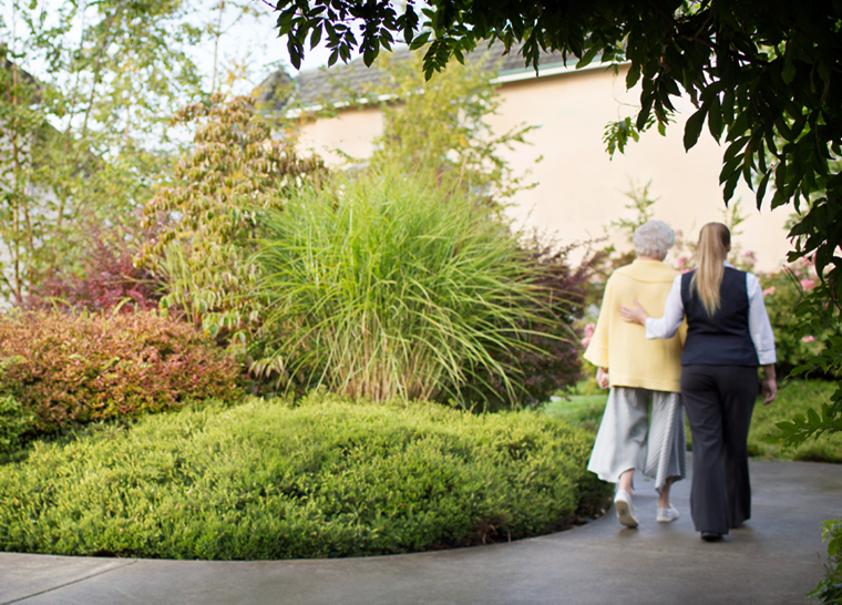 Team member and senior walking in garden at Amica senior living residence.