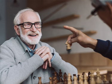 Smiling male Amica senior resident playing chess at Amica residence.