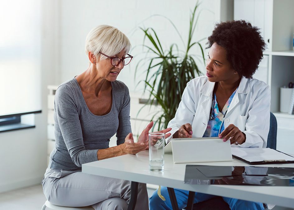 A female doctor sits at her desk and chats to a female caregiver.