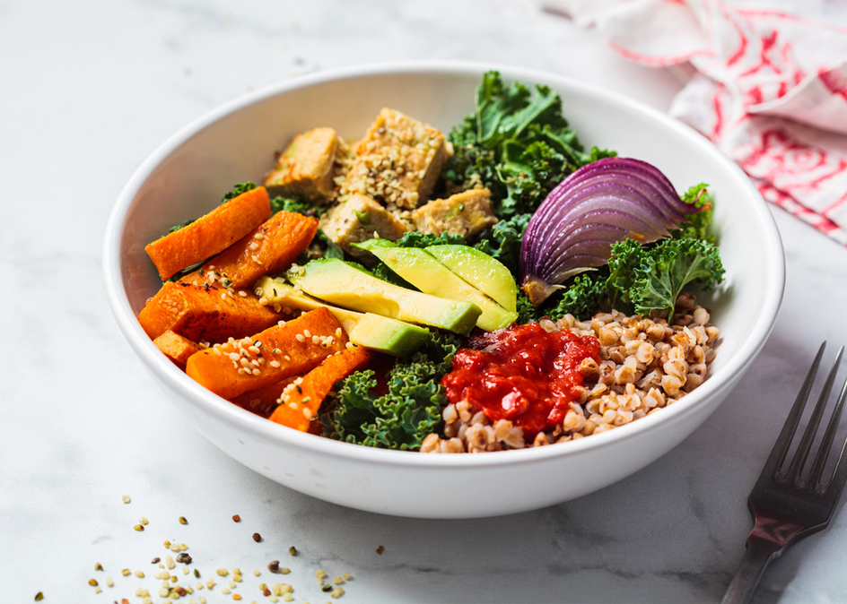 Vegan lunch salad with kale, baked sweet potato, tofu, buckwheat and avocado in a white bowl.