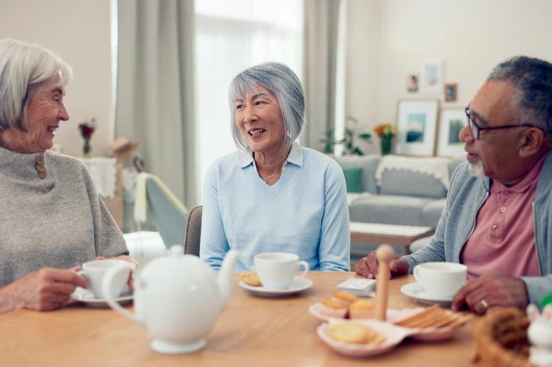 Three seniors drinking tea and snacks sitting around a table, having a conversation.