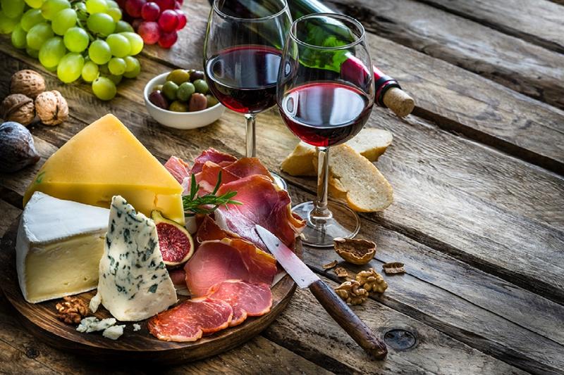 A charcuterie board brimming with good eats sits on wood planks; it's complemented by two glasses of red wine.