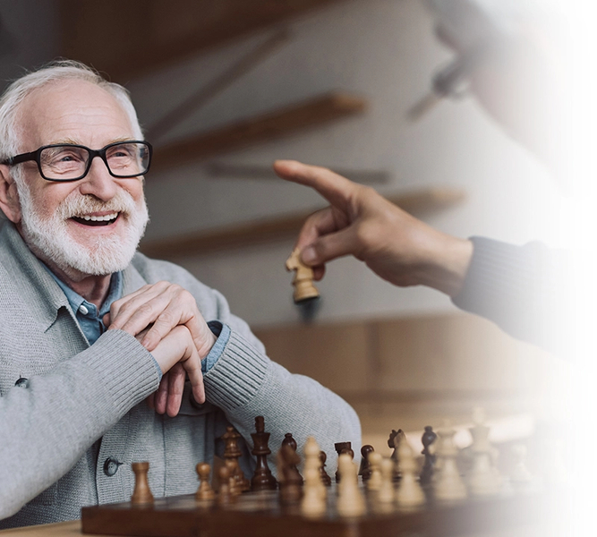 Two senior men play chess. One is seen pointing as he moves his chess piece.