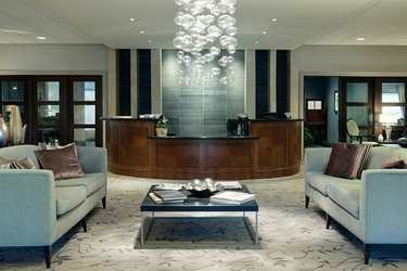 Guests to Amica Thornhill are greeting a lobby adorned with green couches, an elegant coffee table and beautiful lighting.