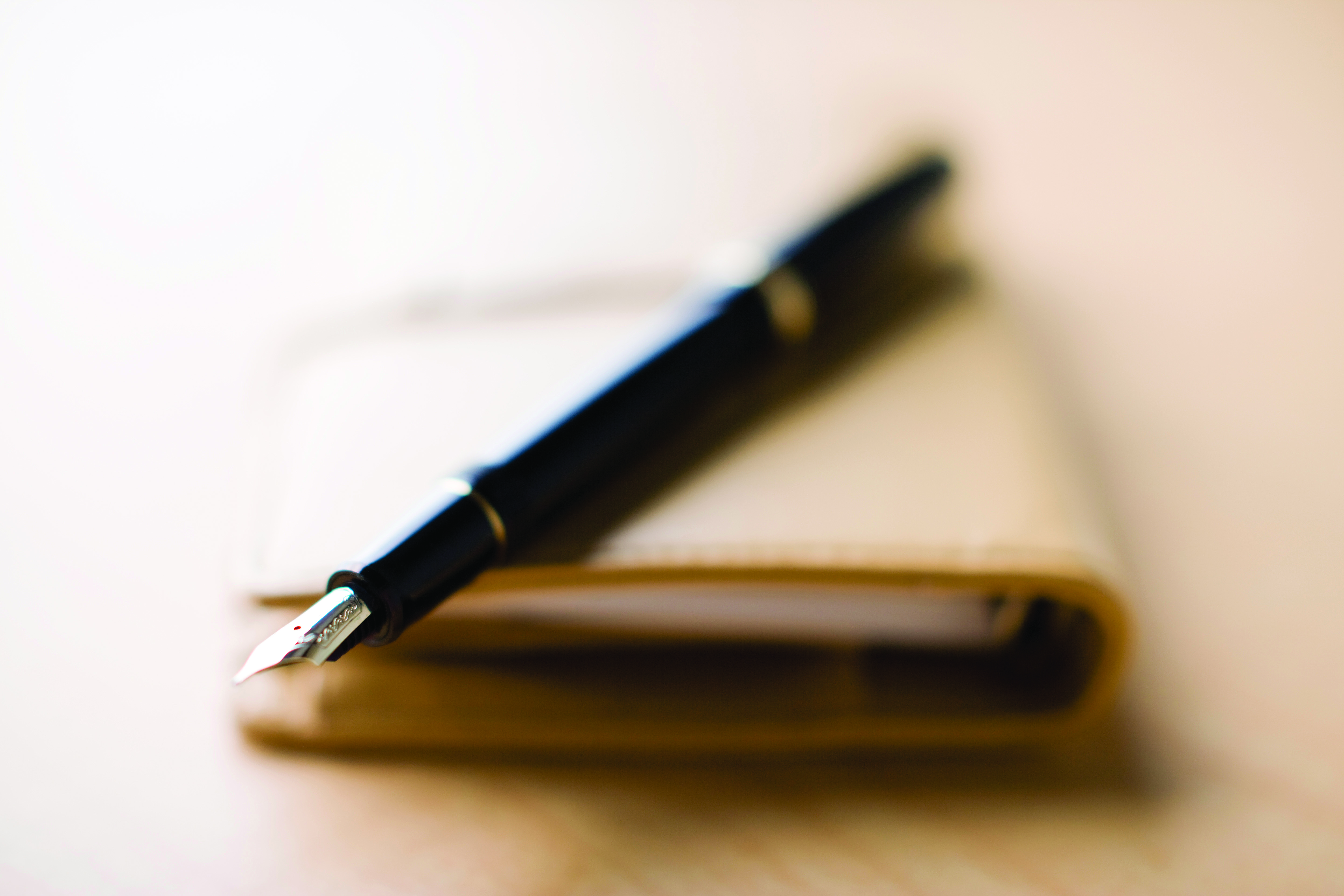 A close up image of a fountain pen sitting on top of a brown journal.