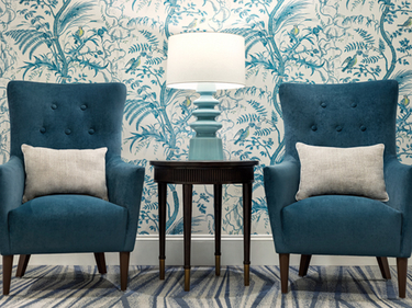 Two plush green chairs with a beige pillow each, flank a small table with lamp.