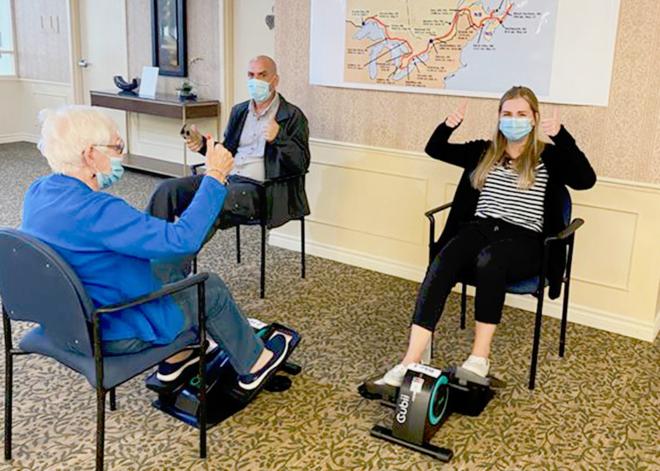 A senior and two young adults stationary cycling indoors.