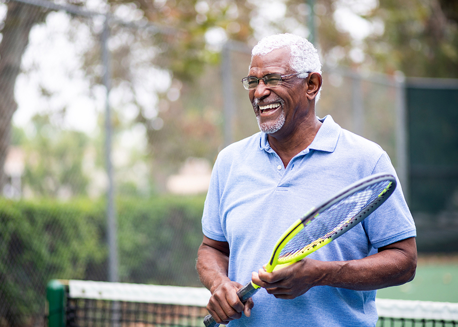 Portrait of a senior man holding a tennis racket in a tennis court outside