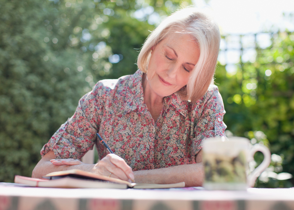 Senior woman writing in her journal, seated at patio table.