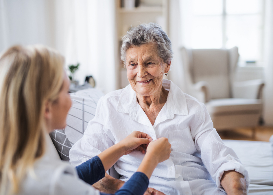 A Team Member helping a happy senior woman sitting on a bed at a residence.