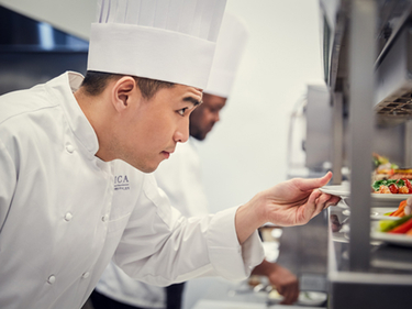 Amica Chef placing a plate of food on the pass in the back-of-house kitchen