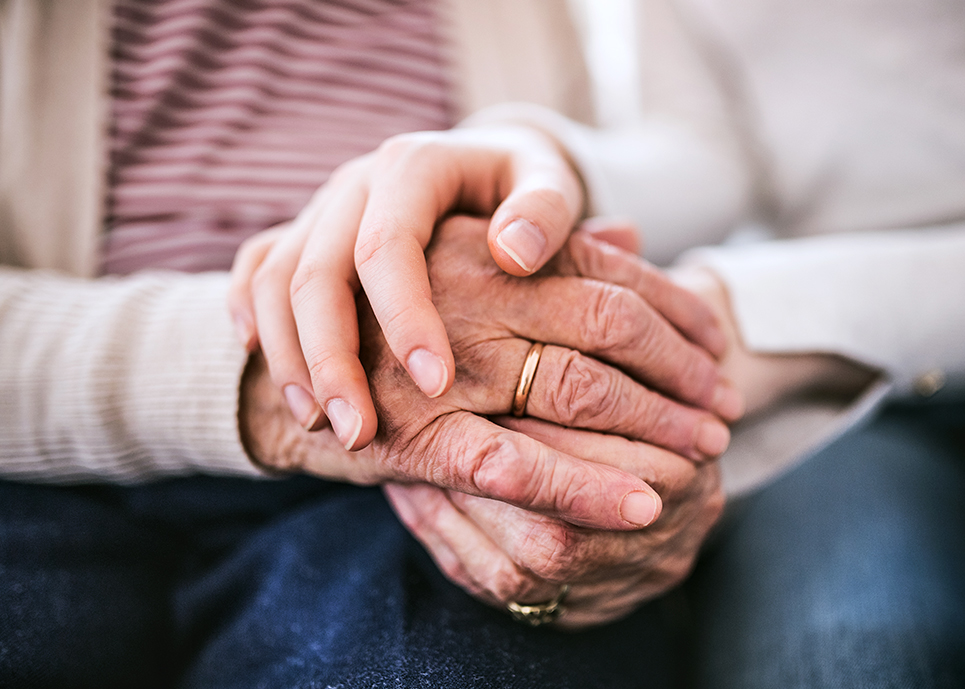 A close-up of a senior woman and young adult holding hands.