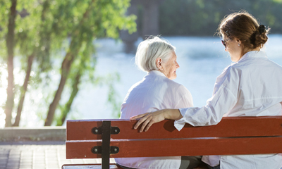 Senior with SDM sitting on bench outside at Amica senior living residence.