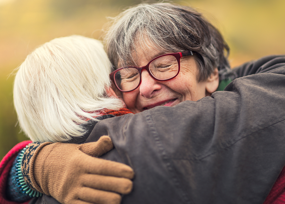 Zoomed in image of a senior woman smiling and hugging another senior.