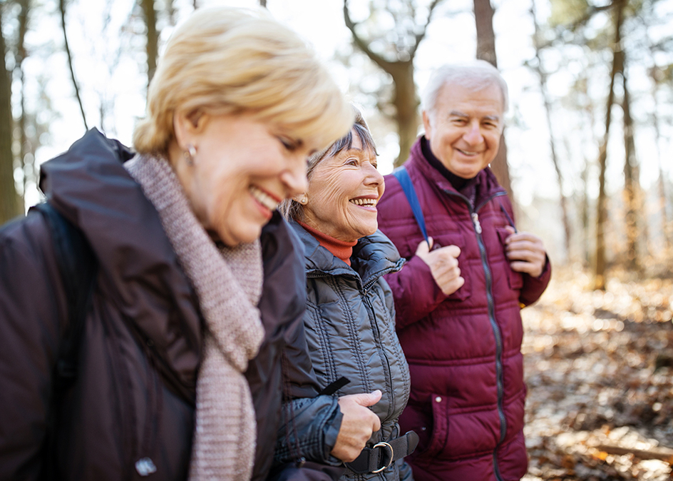 Active seniors on country walk through forest trail on a cold fall day.