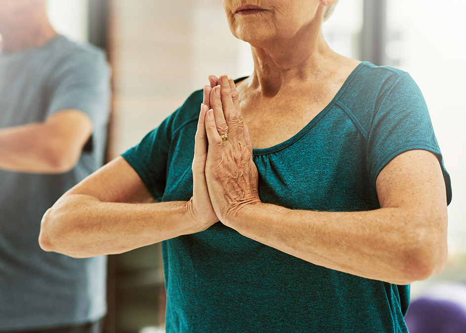 A senior woman sitting cross-legged on a yoga mat, with her palms facing up meditating.