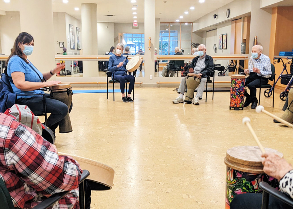 Seniors gathered in a circle, each of them beating a drum.